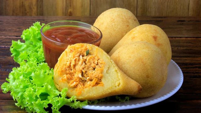Coxinha in the dish, traditional Brazilian cuisine snacks stuffed with chicken, on rustic wooden table. Close up