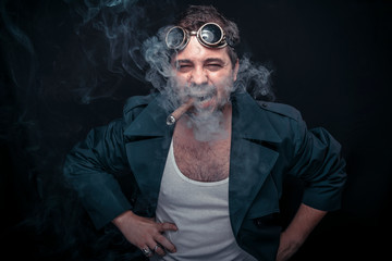 Grunge man, steampunk dressed, smoking a cuban cigar. Black studio background