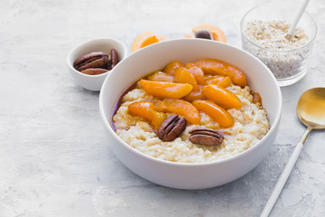 Oatmeal cereal porridge with apricots and pecans in a bowl. Healthy breakfast. Top view on gray stone background.