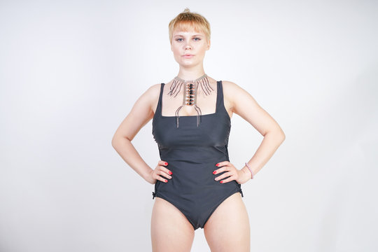 hot curvy chubby woman with short hair and plus size body wearing stylish trendy black swimsuit on white studio background standing alone