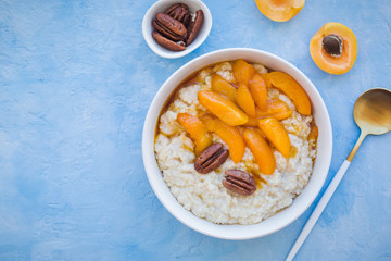 Oatmeal cereal porridge with apricots and pecans in a bowl. Healthy breakfast. Top view on blue stone background.