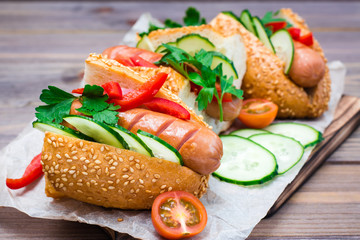 Ready-to-eat hot dogs from fried sausages, sesame buns and fresh vegetables on a cutting board on a wooden table
