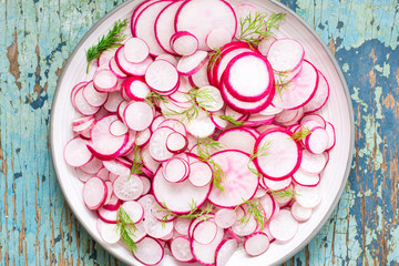 Fresh salad of pieces of radish and dill on a plate on a wooden table. Ready snack for a diet. Top view. Close-up