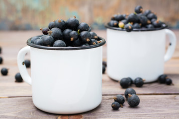 Ripe black currants in metal white mugs on a wooden table. Rustic style