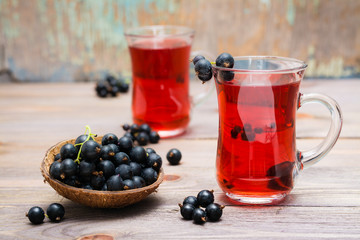 Fresh ripe black currant compote in a glass and a bowl of berries on a wooden table