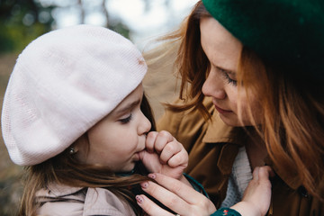 Young mother and little toddler daughter in a beret kissing each other in the autumn forest.