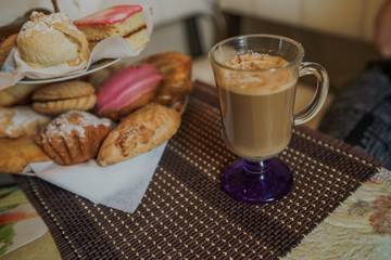 Food photography. Hot cappuccino with different homemade pastries in a basket on the table in fast food cafe.