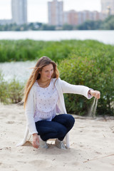 Attractive young woman is sitting on the sand and pours sand from her hand. Lifestyle concept....