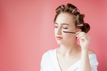 nice cheerful young the girl in the curler paints an eyebrow on pink background