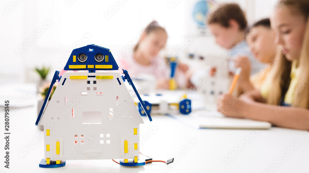Poster handmade robot at desk with schoolchildren at background