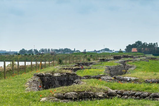 Diksmuide, Flanders, Belgium -  June 19, 2019: Overview of Historic WW1 Trenches, called Dodengang along IJzer River, shows gray-brown stone-hard sandbags, green grass, red poppies. Barbed wire fence 