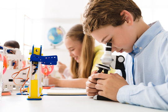 Boy looking at microscope with robot nearby