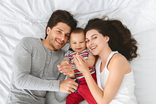 Young Millennial Parents Embracing With Baby Son In Bed