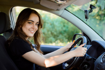 Fototapeta na wymiar Attractive cheerful girl driver sits in the driver's seat of a modern car and looks to the camera with broad smile