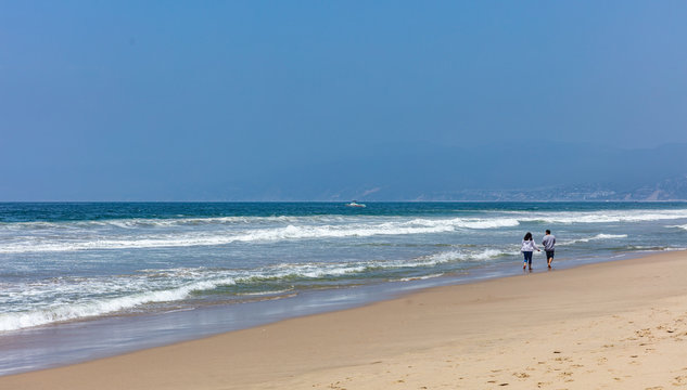 Young couple walking on the sandy beach. Blue ocean sea waves, clear blue sky in a sunny spring day