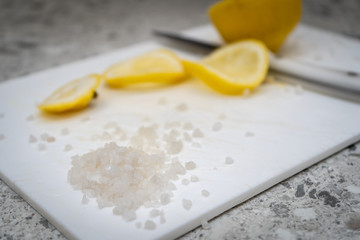 Scattered sea salt and fresh juicy yellow lemon cut in half and into slices on a cutting board next to a knife on the kitchen table. Side view