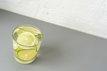 A glass of a refreshing drink, a cocktail with sliced ​​lime on the left on the light grey table. Copy space. Diagonal background