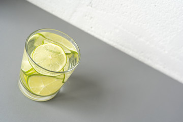 Close-up. A glass of a refreshing drink, a cocktail with sliced ​​lime on the left on the light grey table. Copy space. Diagonal background