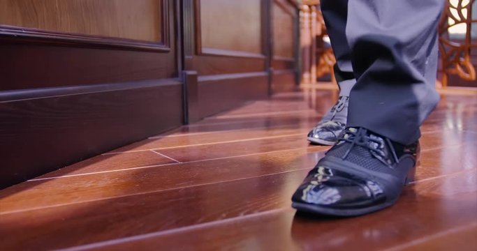 Close-up men's feet and black shoes. Business guy walks over a wooden floor in a chic office.