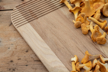 Yellow mushrooms chanterelle (cantharellus cibarius) on a vintage cutting board and a wooden kitchen table and copy space for text.