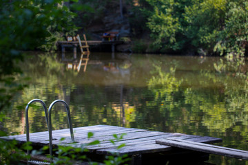 Fototapeta na wymiar wooden pier with a swimming ladder in a scenic lush green lake surrounded by trees