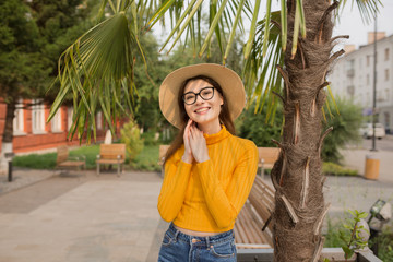 woman in the city is having fun, laughing. Palm trees in the background. Bright yellow clothes, glasses, hat. Summer street photography