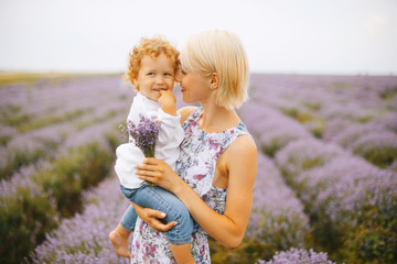 Young mother is holding her child and smiling in the middle of lavender field.