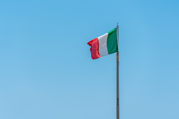 an Italian flag blowing in the wind against a bright blue sky