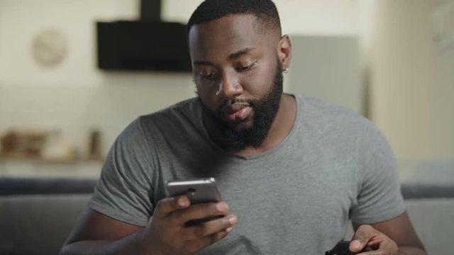Black man holding phone at kitchen. Closeup young adult texting in smartphone.