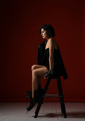 Tense overwrought woman in black tight dress, leather jacket and big brutal boots sitting on a...