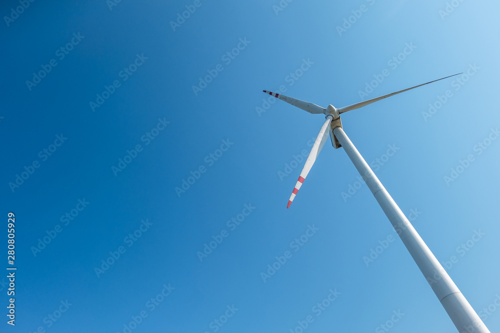 Wall mural rotating blades of a windmill propeller on blue sky background. wind power generation. pure green en