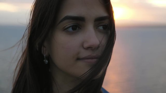 Dainty brunette girl standing at Black Sea beach at sunset in summer in slo-mo 