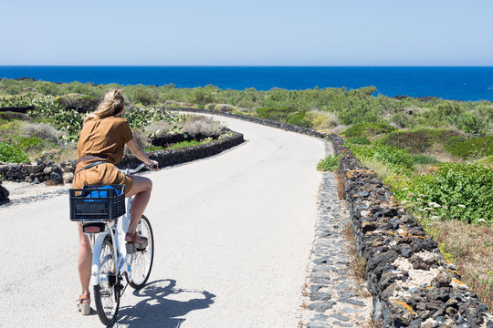 Blonde girl riding bike near seaside on summer at Linosa Island near Lampedusa Island Sicily Italy 