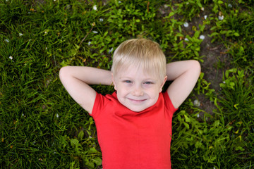 Portrait of a smiling blond boy lying on the grass. Hands behind head. Rest at nature