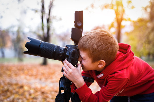 Portrait of schoolboy takes pictures on a SLR camera. Autumn Park