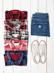 Clothing concept. Plaid shirts, blue jeans and white sneakers on a white wooden background. Top view