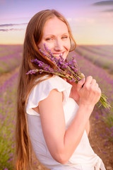 closeup portrait of a beautiful woman with a lavender flower bouquet into purple lavender fields during a summer sunset - Image