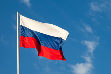 Russian flag  close-up on a pole against a blue sky. The Russian flag develops in a wave in the wind.