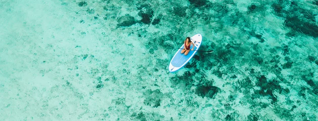 Woman sitting on sup board and enjoying turquoise transparent water and coral reef. Tropical travel, wanderlust and water activity concept. © Oleg Breslavtsev