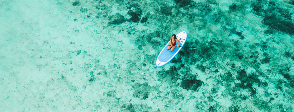 Woman sitting on sup board and enjoying turquoise transparent water and coral reef. Tropical travel, wanderlust and water activity concept.