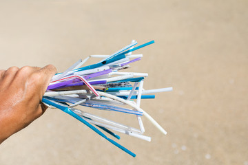 Hand holding heap of used plastic straws on background of clean beach and ocean waves. Plastic ocean pollution, environmental crisis. Say no plastic. Single-use plastic waste