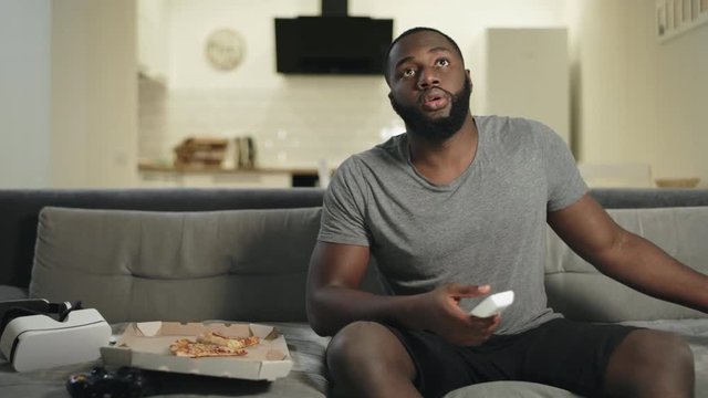 African man searching tv program at home. Smiling man reading message at phone
