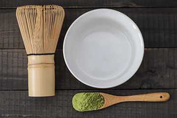 Green matcha tea powder lies in a wooden spoon. in the background is a white cup for this tea and a whisk