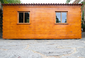 Simple wooden cabin with windows and roof in corrugated iron, surrounded by palms, front view.