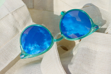 Women's sunglasses with reflective summer blue sky and clouds lying on canvas