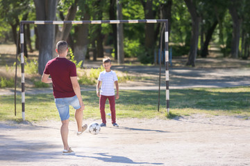 Little boy with his dad playing football on soccer pitch