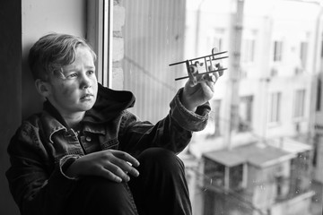 Homeless little boy playing with airplane near window indoors