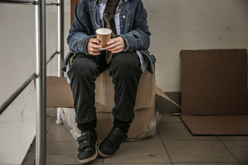 Homeless little boy with cup sitting indoors