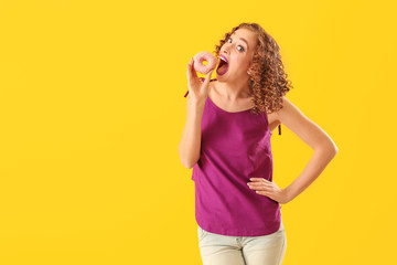 Beautiful young woman eating tasty doughnut on color background