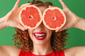 Happy young woman with tasty grapefruit on color background
